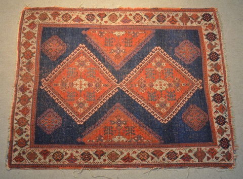 Pequea alfombra oriental con dos rombos bord, sobre fondo azul. 126 x 101 cm.